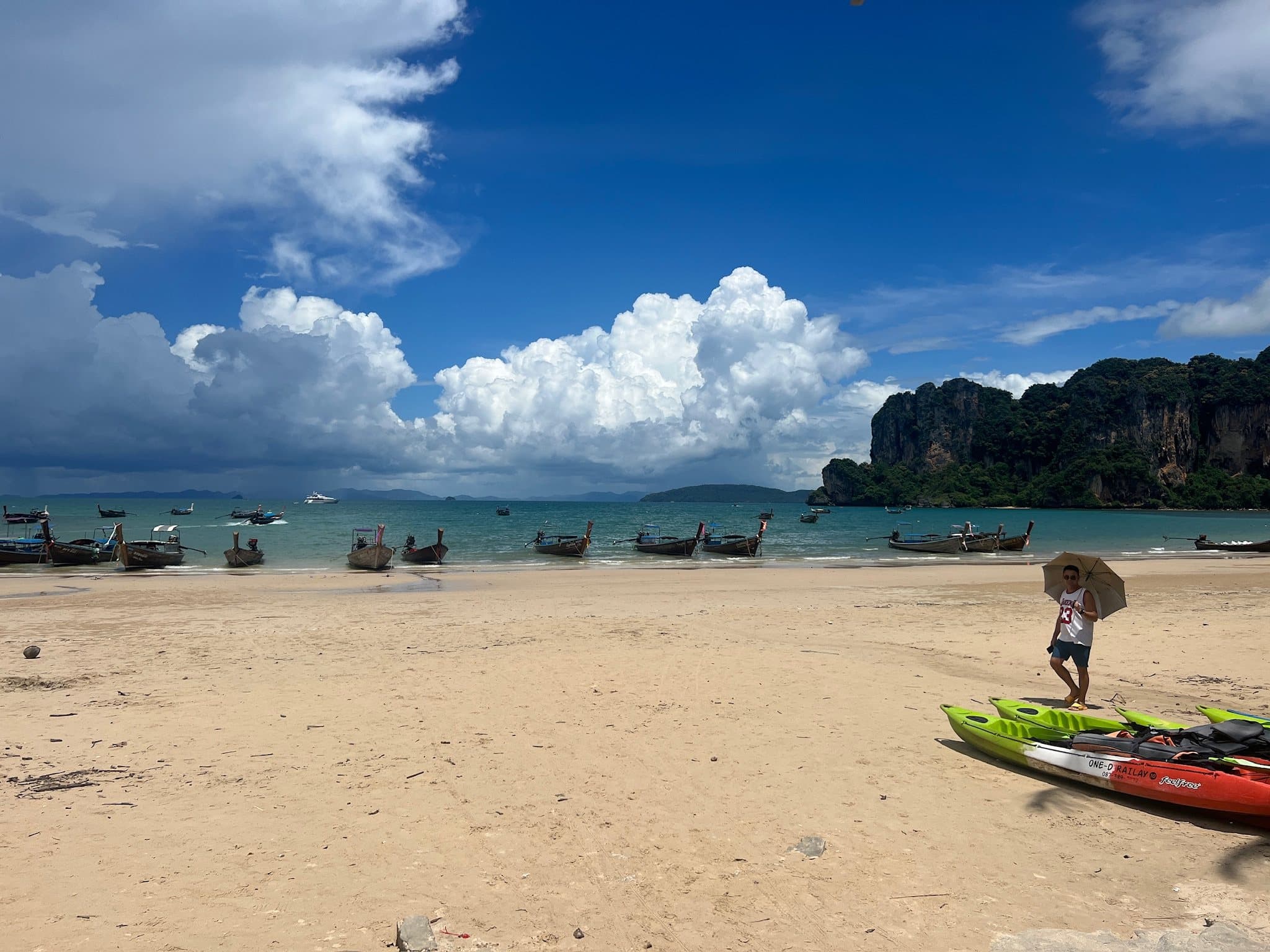 Longtail boats moored off Ao Nang beach, with limestone cliffs behind and a kayak pulled up on the sand
