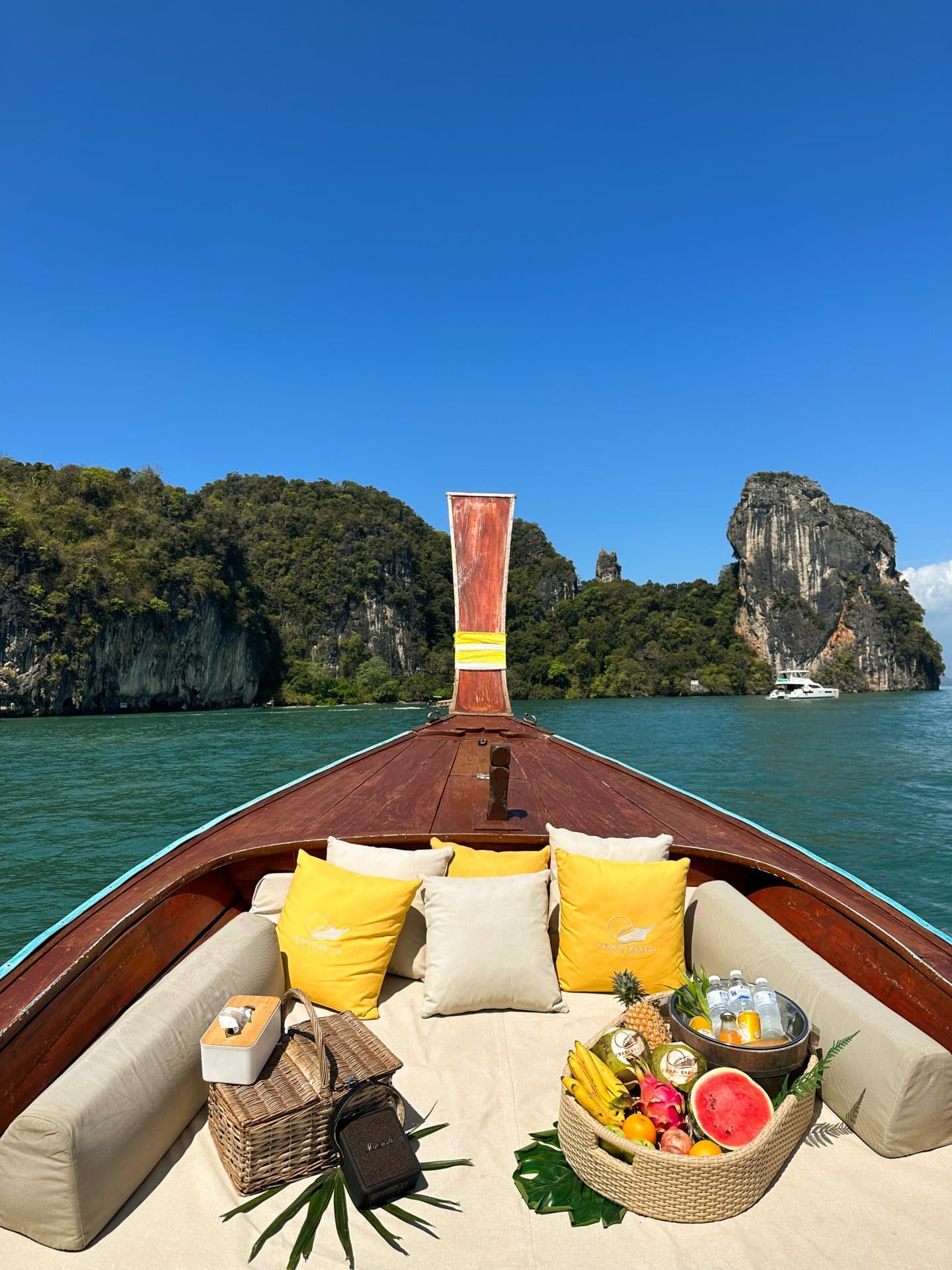 The bow of a longtail boat set with cushions and a fruit platter, heading towards limestone islands